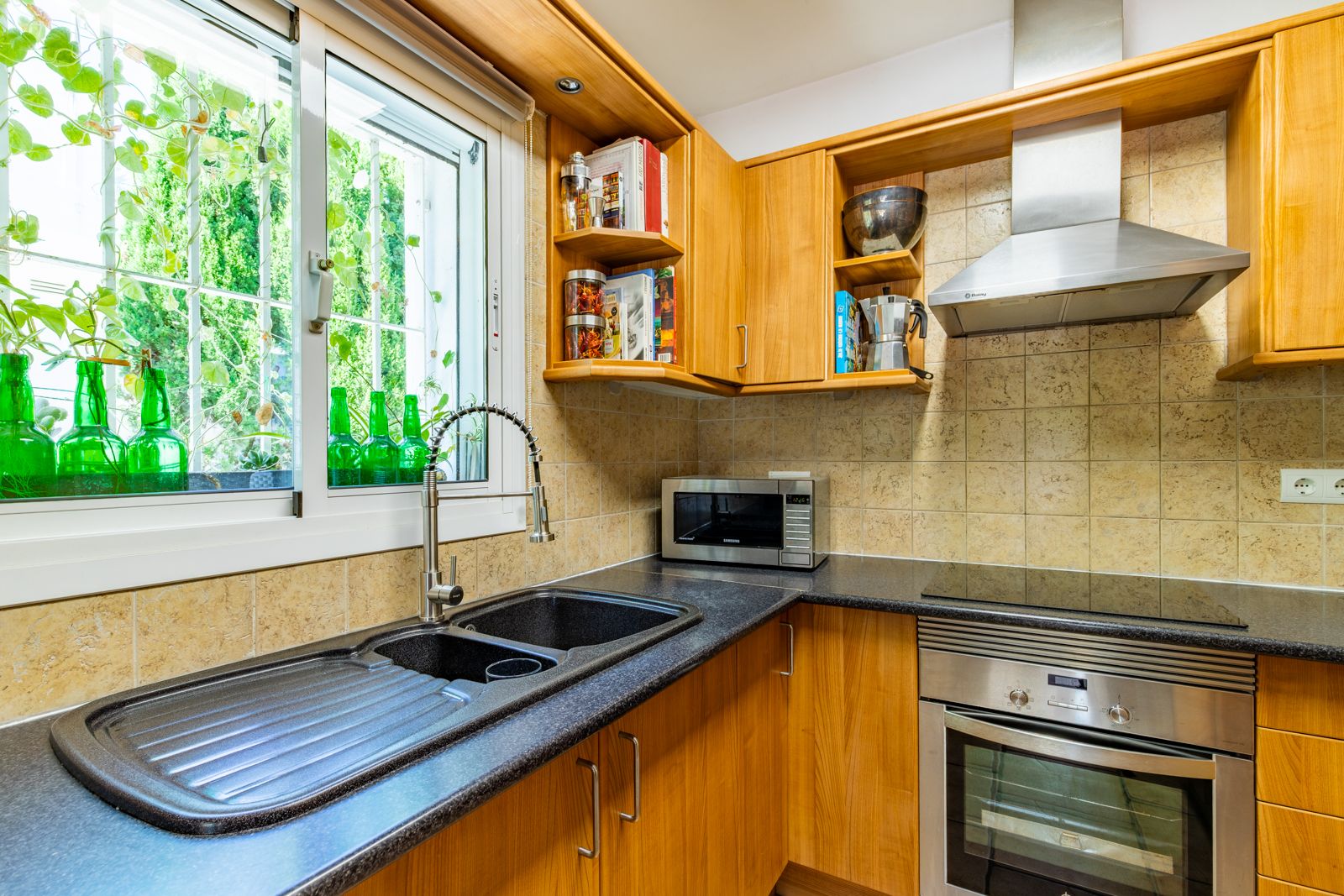 Ausgestattete Küche mit Holzschränken, dunkler Granitarbeitsplatte und Doppelspüle. Mit Edelstahlgeräten und natürlichem Licht durch das Gartenfenster.