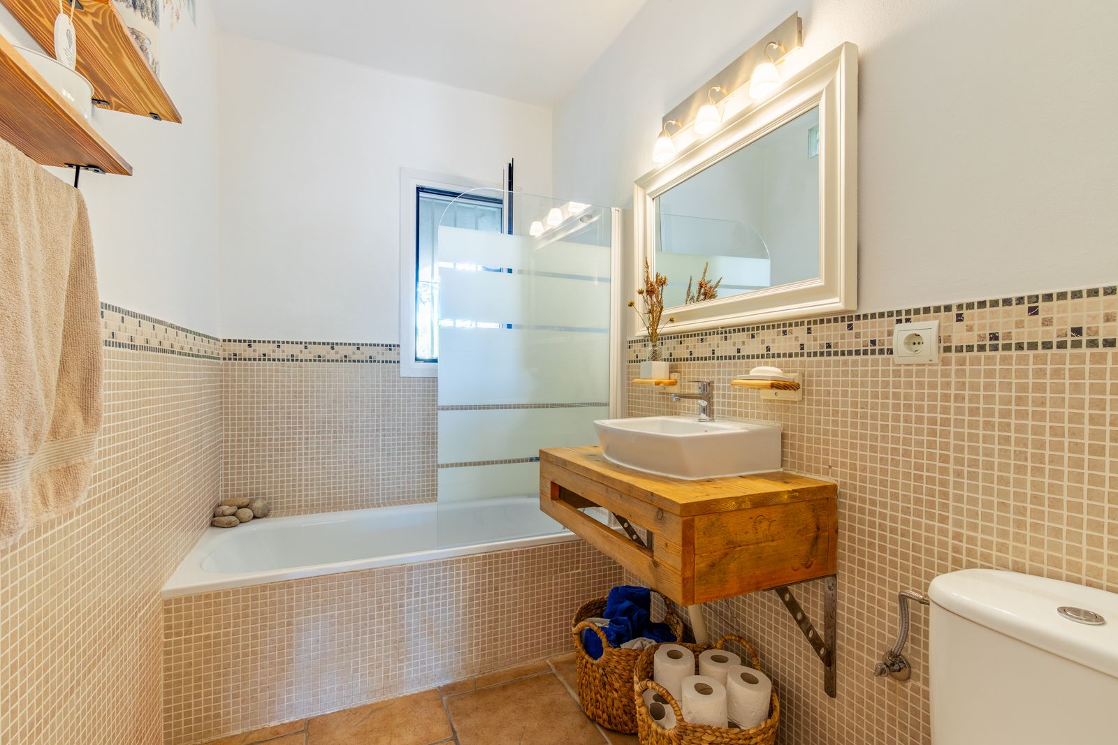 Badezimmer im rustikalen Stil mit Massivholz-Waschtisch, Aufsatzwaschbecken, Badewanne mit Glasabtrennung und beigen Mosaikfliesen.