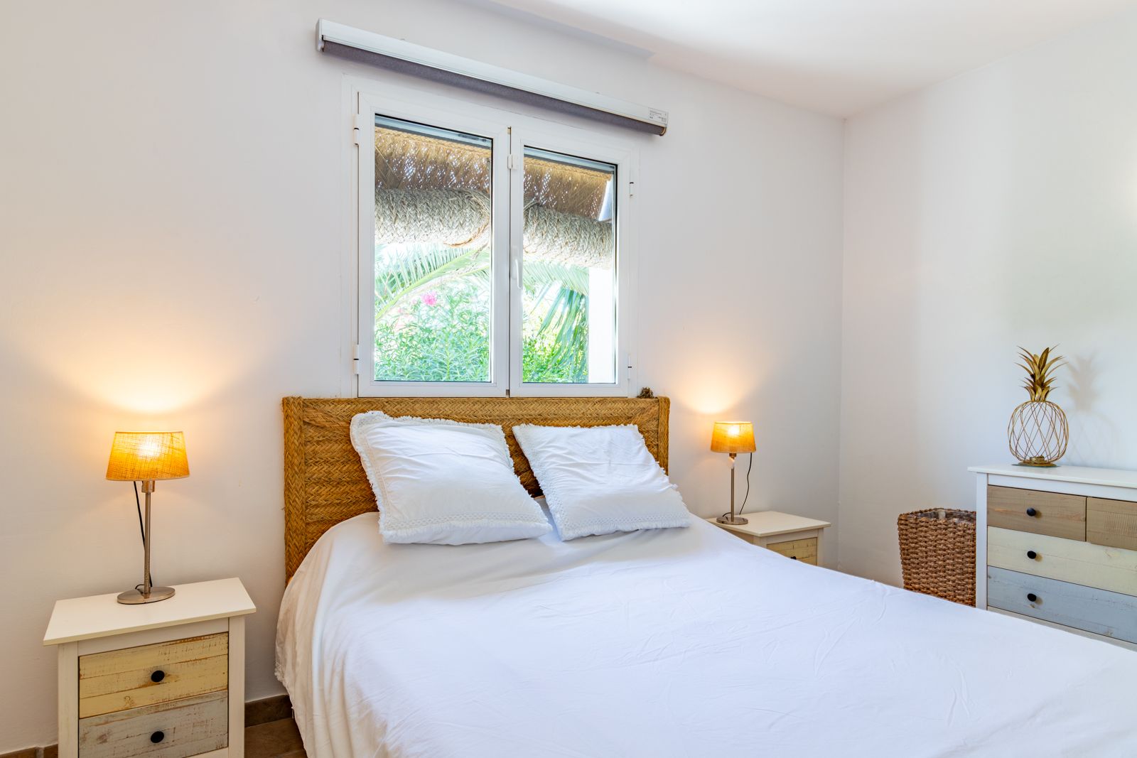 Doppelzimmer mit geflochtenem Kopfteil, rustikalen Holznachttischen und Gartenblick. Ein heller Raum mit mediterranem Charme.