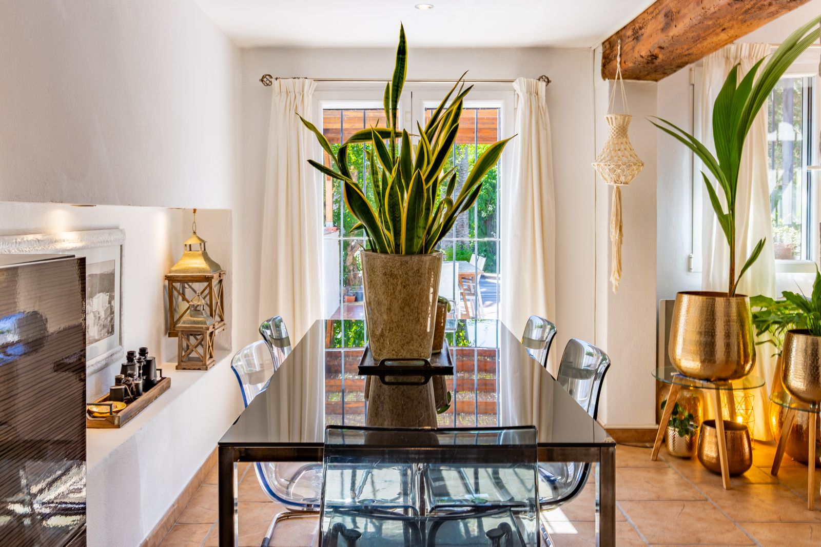 Heller Essbereich mit Glastisch, transparenten Stühlen und sichtbaren Holzbalken. Große Fenstertüren führen direkt auf die Terrasse und in den Garten.