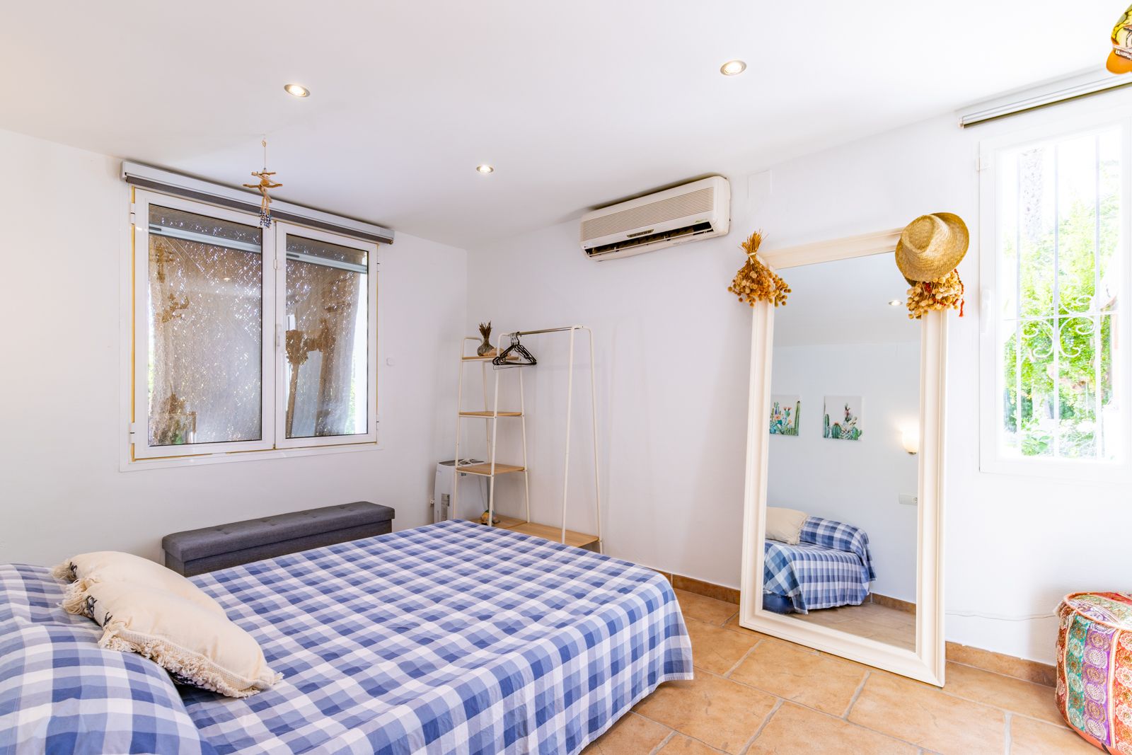Helles Schlafzimmer mit Terrakottaboden, Klimaanlage und einem großen Standspiegel. Einbaustrahler und natürliches Licht sorgen für eine angenehme Atmosphäre.