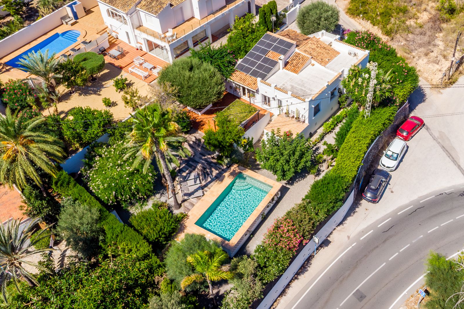 Luftaufnahme der Villa mit dem rechteckigen Pool, dem üppigen mediterranen Garten und der Solaranlage auf dem traditionellen Ziegeldach.
