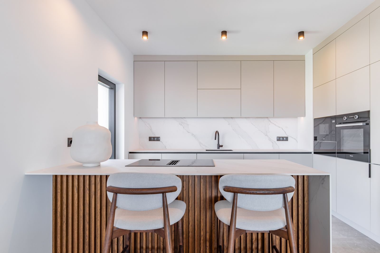 Designerküche mit einer Insel aus Eichenlamellen, Arbeitsplatten aus gesintertem Stein und integrierten Miele-Geräten in minimalistischen Schränken.