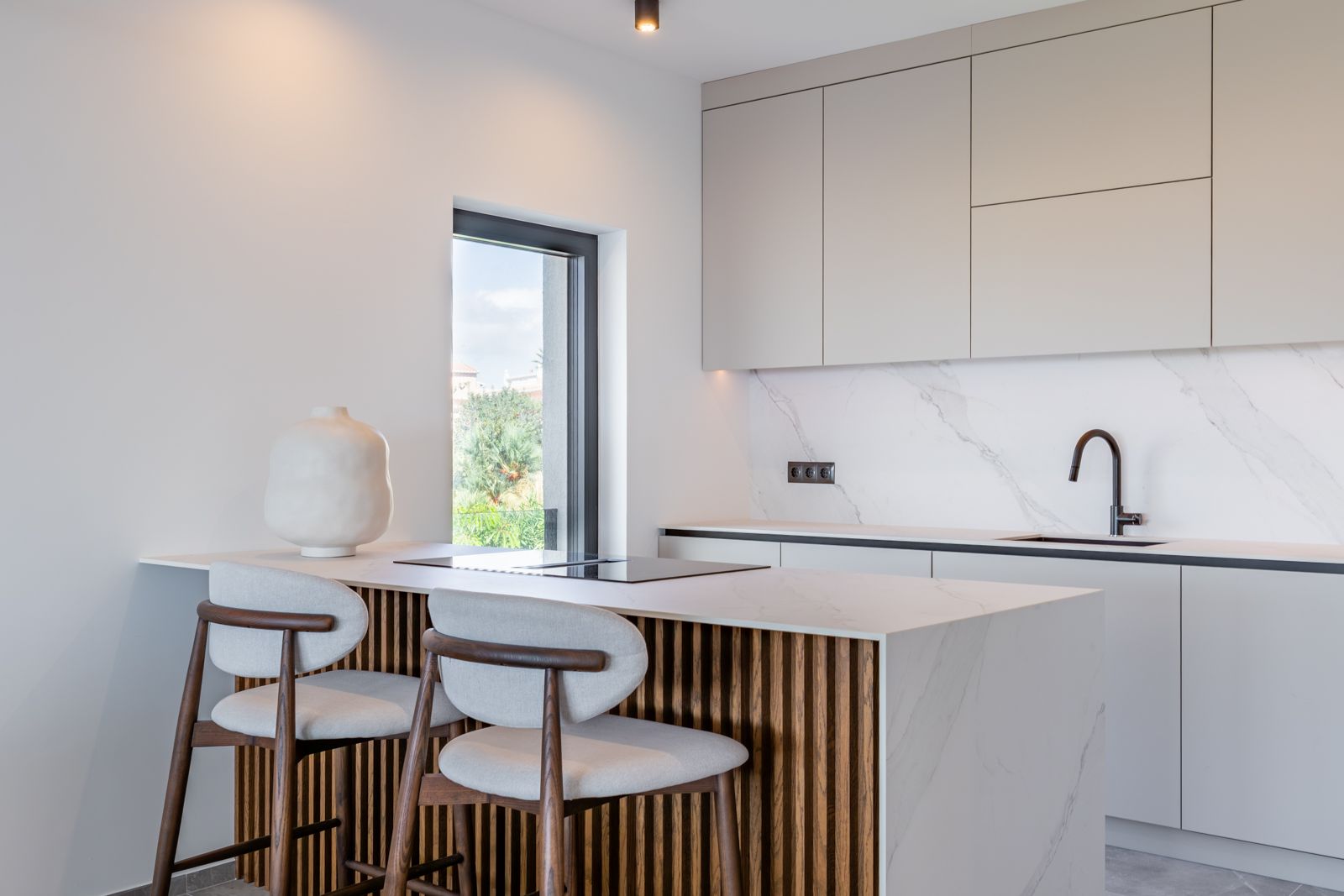 Designerküche mit Kochinsel aus gesintertem Stein in Marmoroptik, Holzlamellen-Verkleidung und integriertem Induktionsfeld. Elegante Barhocker ergänzen das minimalistische Ambiente.