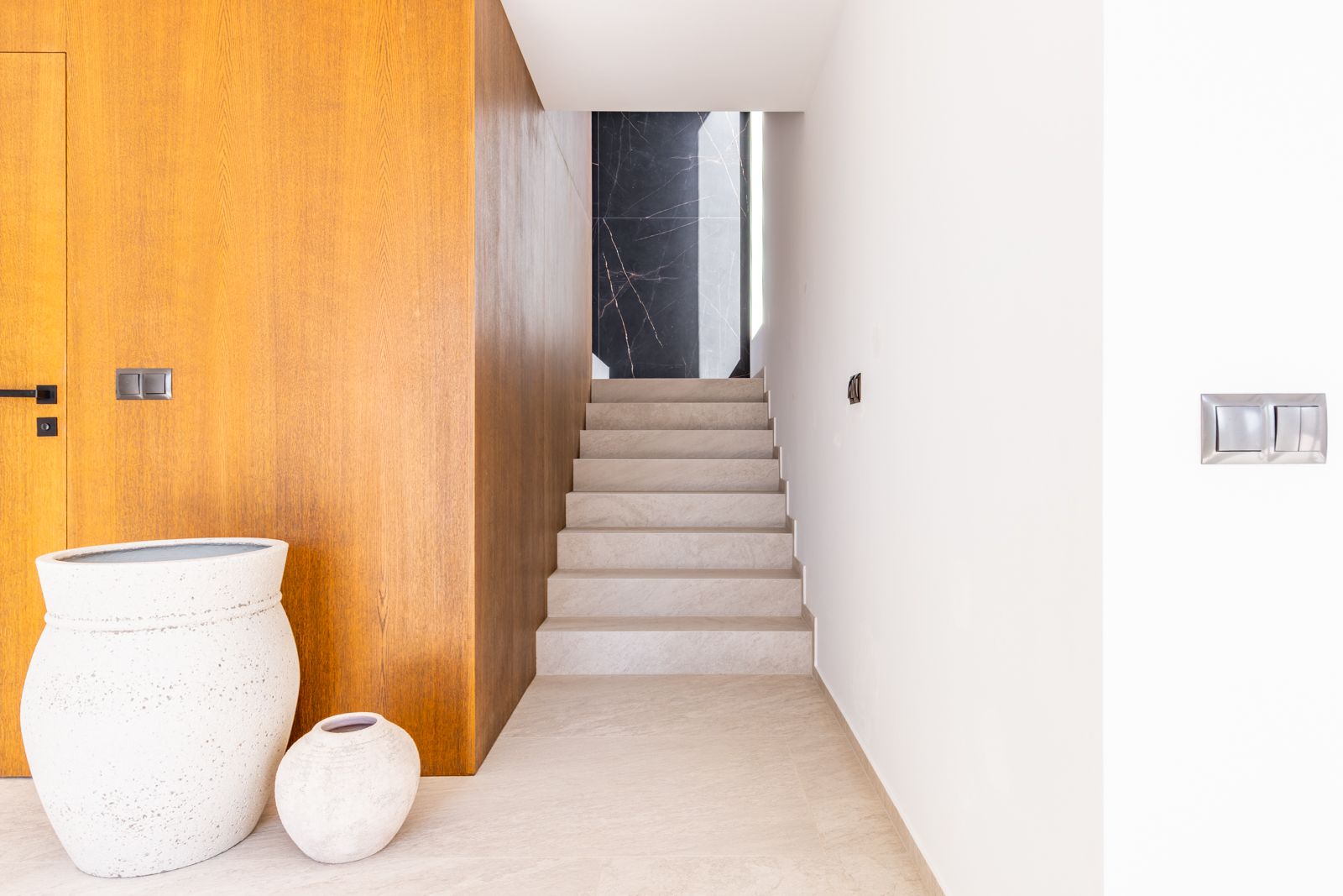 Flur mit Feinsteinzeug-Treppe, Wandverkleidung aus Natureiche und einer Akzentwand aus schwarzem gesintertem Stein mit weißer Maserung.