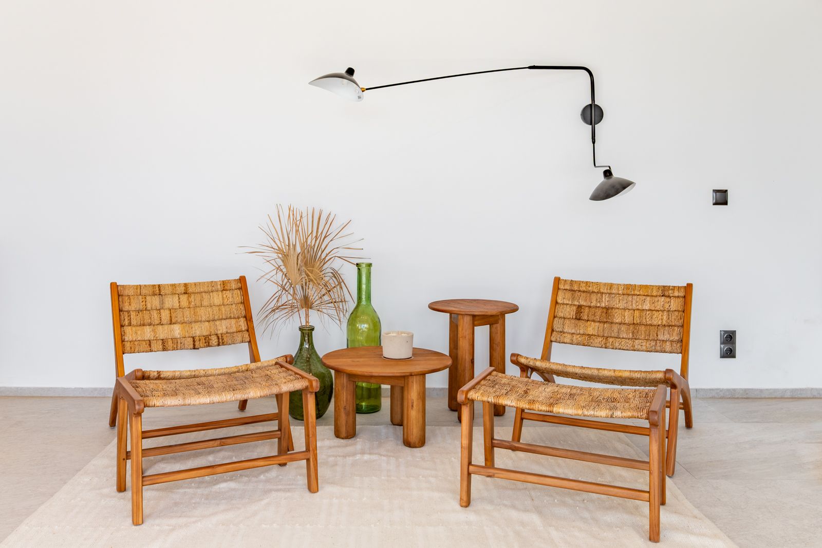 Loungebereich mit Holzsesseln und Naturfasergeflecht, Beistelltischen aus Teak und einer schwarzen Designer-Wandleuchte auf hellem Feinsteinzeug.