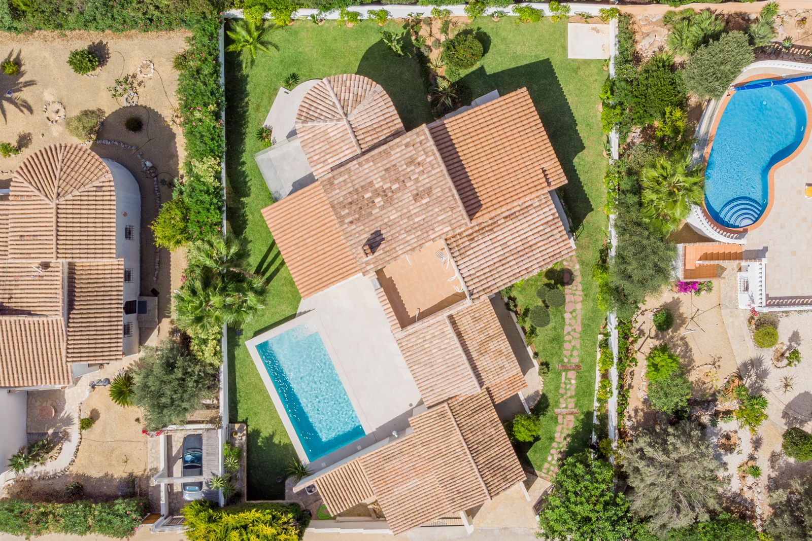 Luftaufnahme der Villa mit Blick auf die Dachlandschaft aus Terrakotta-Ziegeln, den rechteckigen Pool und den gepflegten Garten mit Rasenflächen.