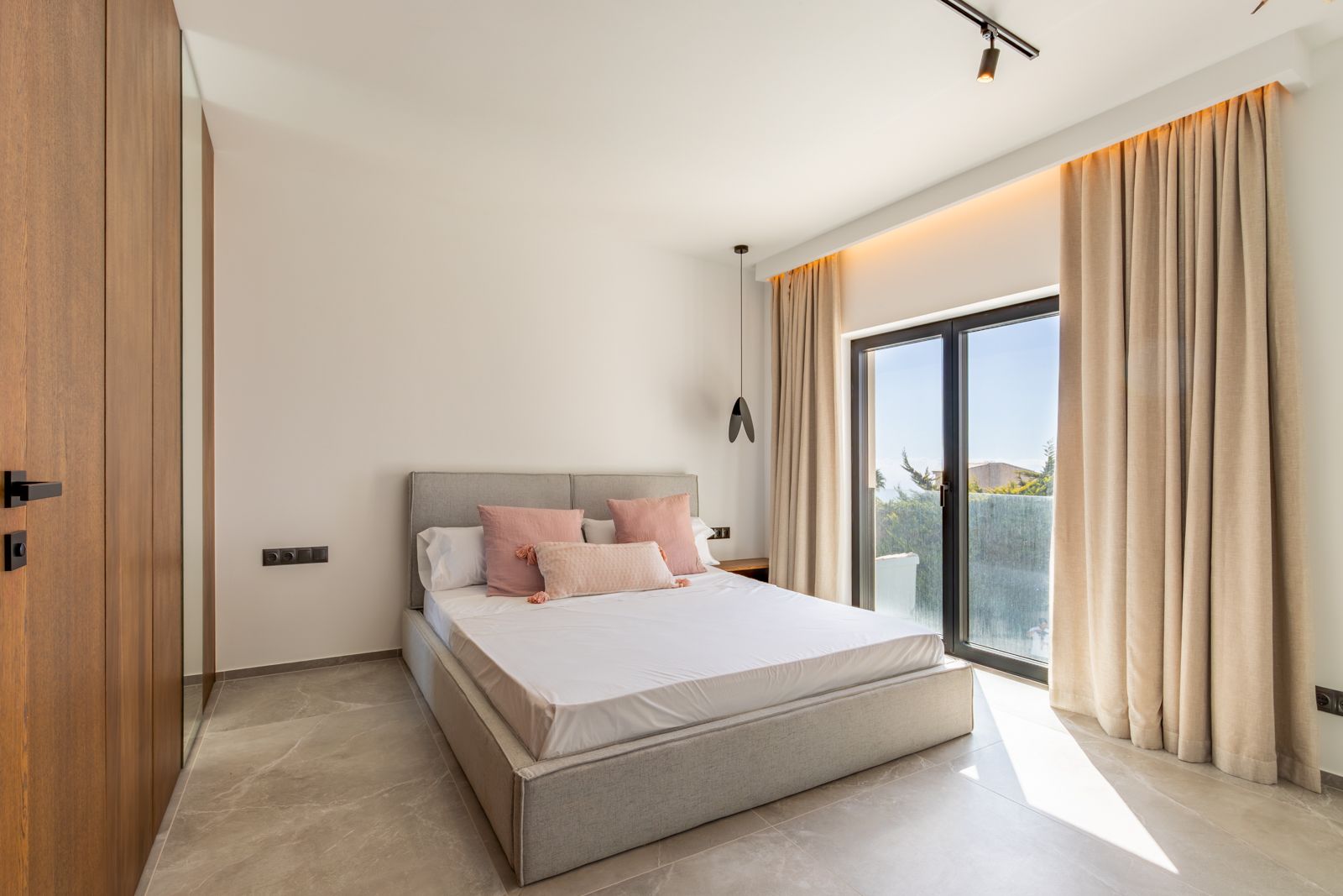 Modernes Schlafzimmer mit großformatigen Feinsteinzeugfliesen, maßgefertigten Eichenschränken mit Spiegel und direktem Zugang nach draußen durch hochwertige Glasfronten.