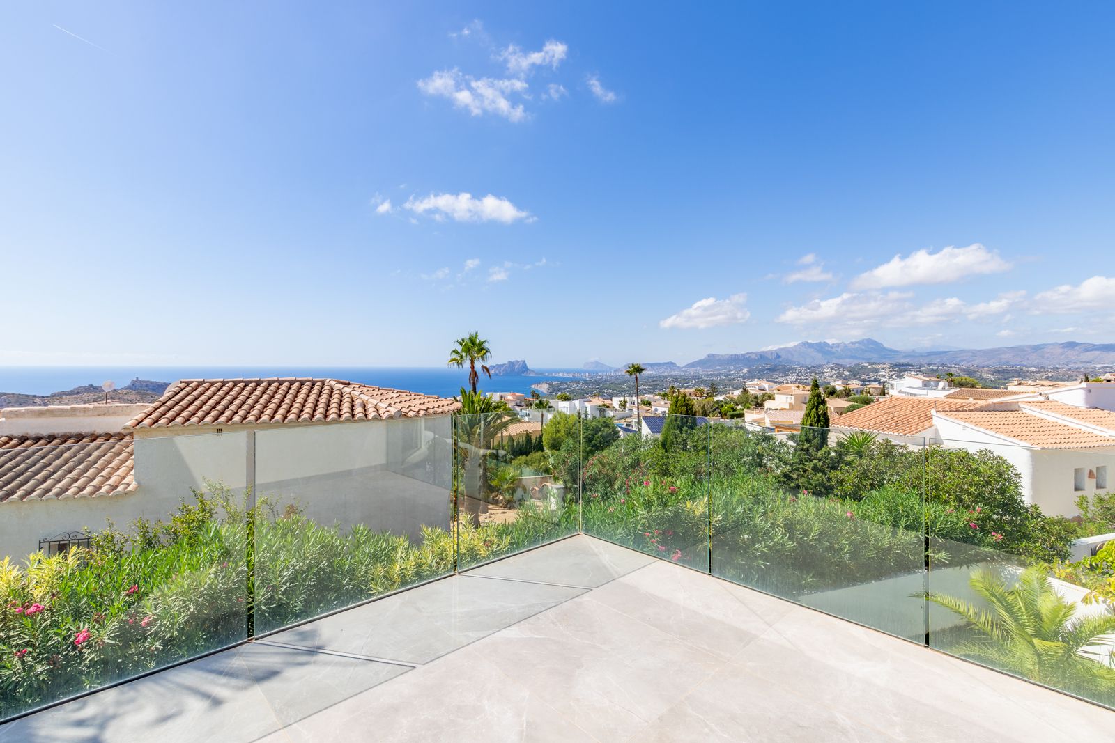 Obere Terrasse mit großformatigen Feinsteinzeugfliesen und Glasgeländer, die einen Panoramablick auf das Mittelmeer und den Peñón de Ifach bietet.