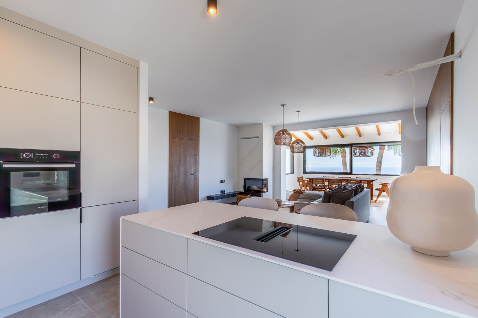Offene Designerküche mit Kochinsel aus gesintertem Stein, integriertem Induktionsfeld, Miele-Geräten und fließendem Übergang zum Wohnbereich mit Meerblick.