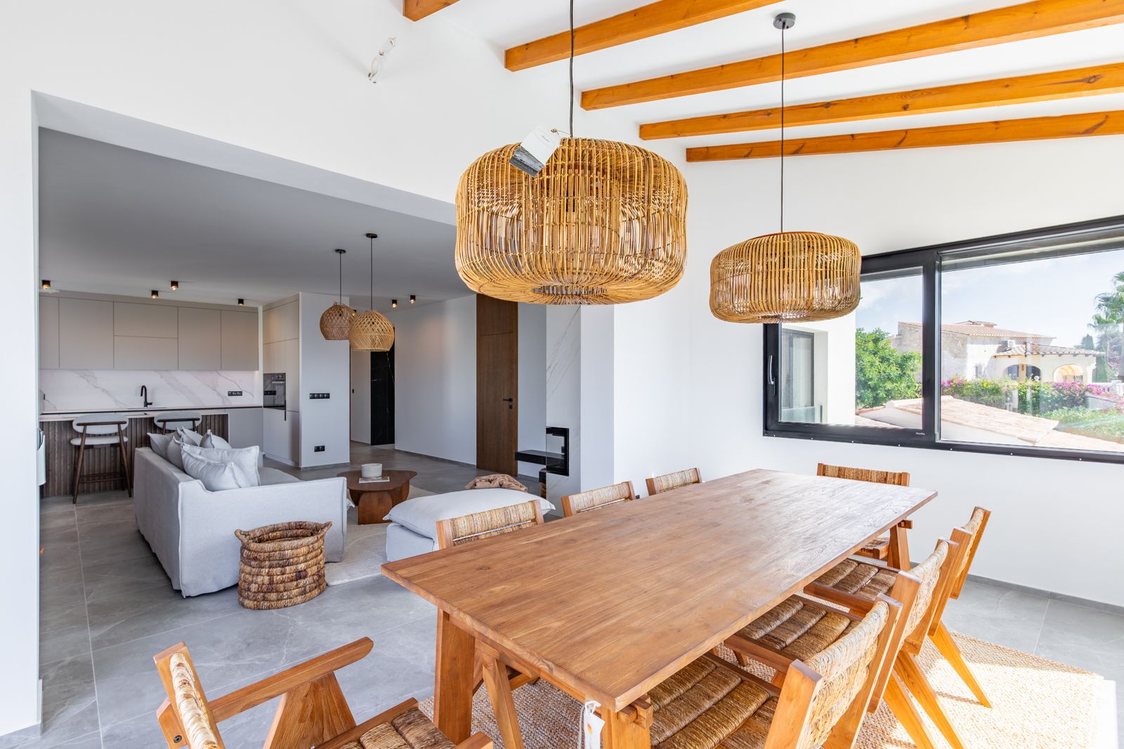 Offener Essbereich mit Massivholztisch, Sichtbalken und Rattan-Pendelleuchten, der fließend in das Wohnzimmer und die moderne Küche übergeht.
