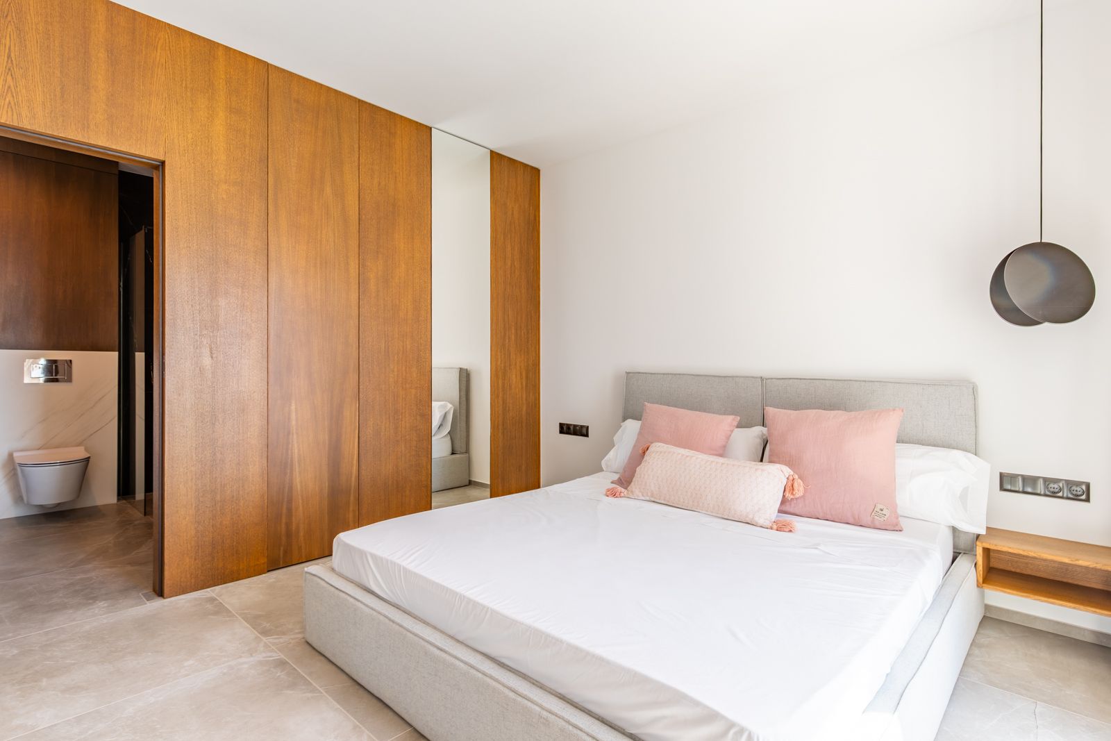 Schlafzimmer mit maßgefertigten Eichenholzfronten, großformatigem Feinsteinzeug und direktem Zugang zum En-Suite-Bad mit Marmoroptik.