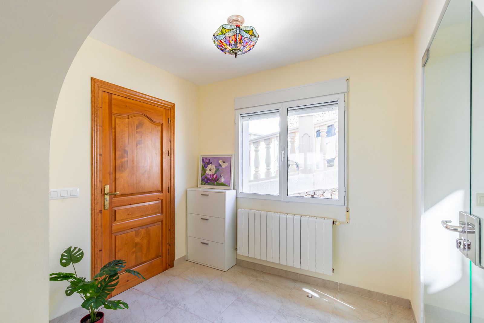 Eingangsbereich mit Massivholztür, Zentralheizungskörper und einer Tiffany-Deckenleuchte, gestaltet mit hellen Fliesenböden und natürlichem Lichteinfall.