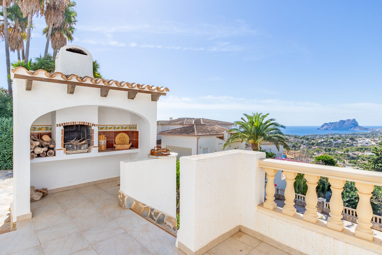 Gemauerter Grillbereich mit Kamin und dekorativen Fliesen auf einer Terrasse mit Panoramablick auf das Mittelmeer und den Peñón de Ifach.