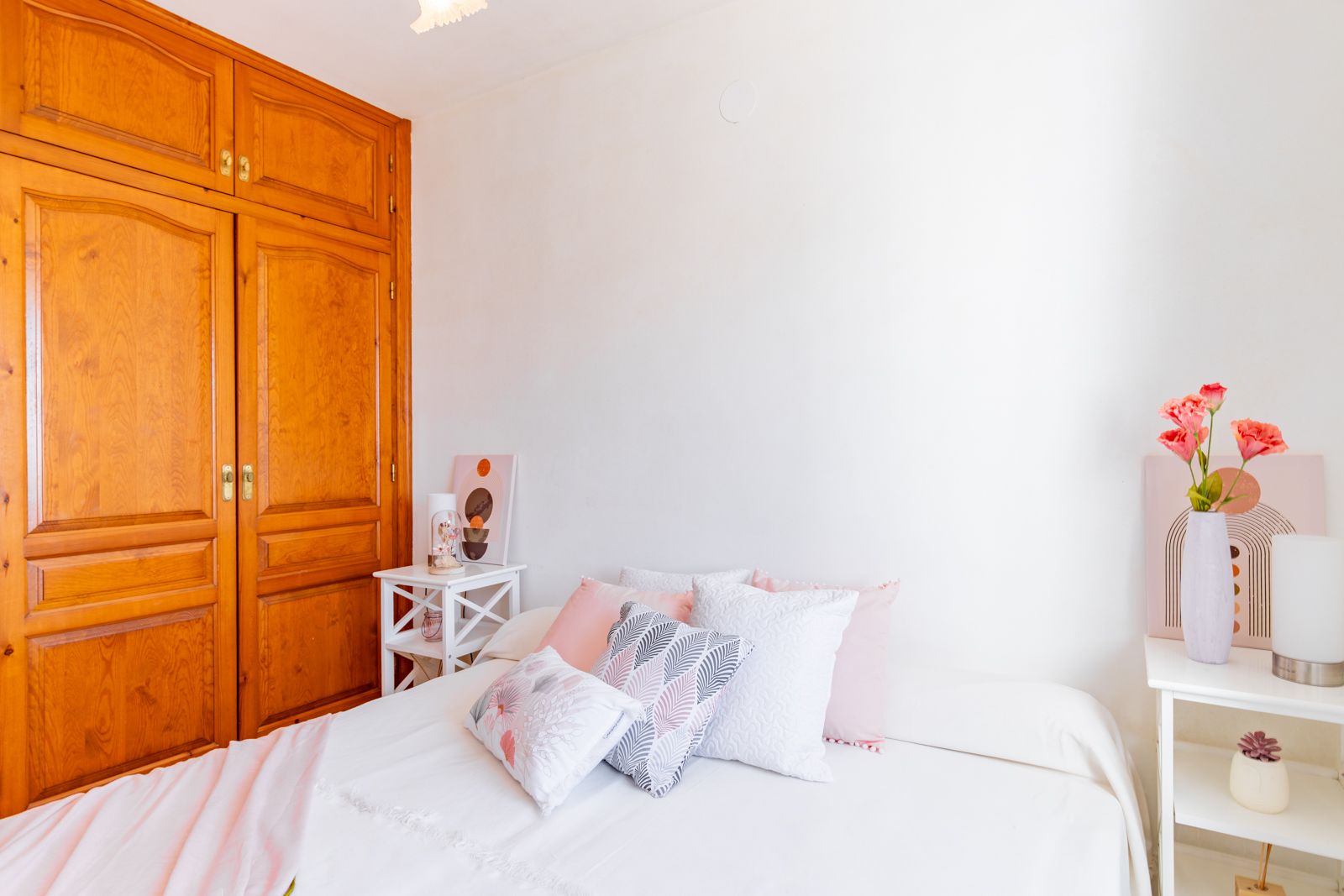 Helles Schlafzimmer mit einem großen Einbauschrank aus Massivholz, weißen Wänden und schlichten Beistelltischen für ein funktionales und warmes Ambiente.