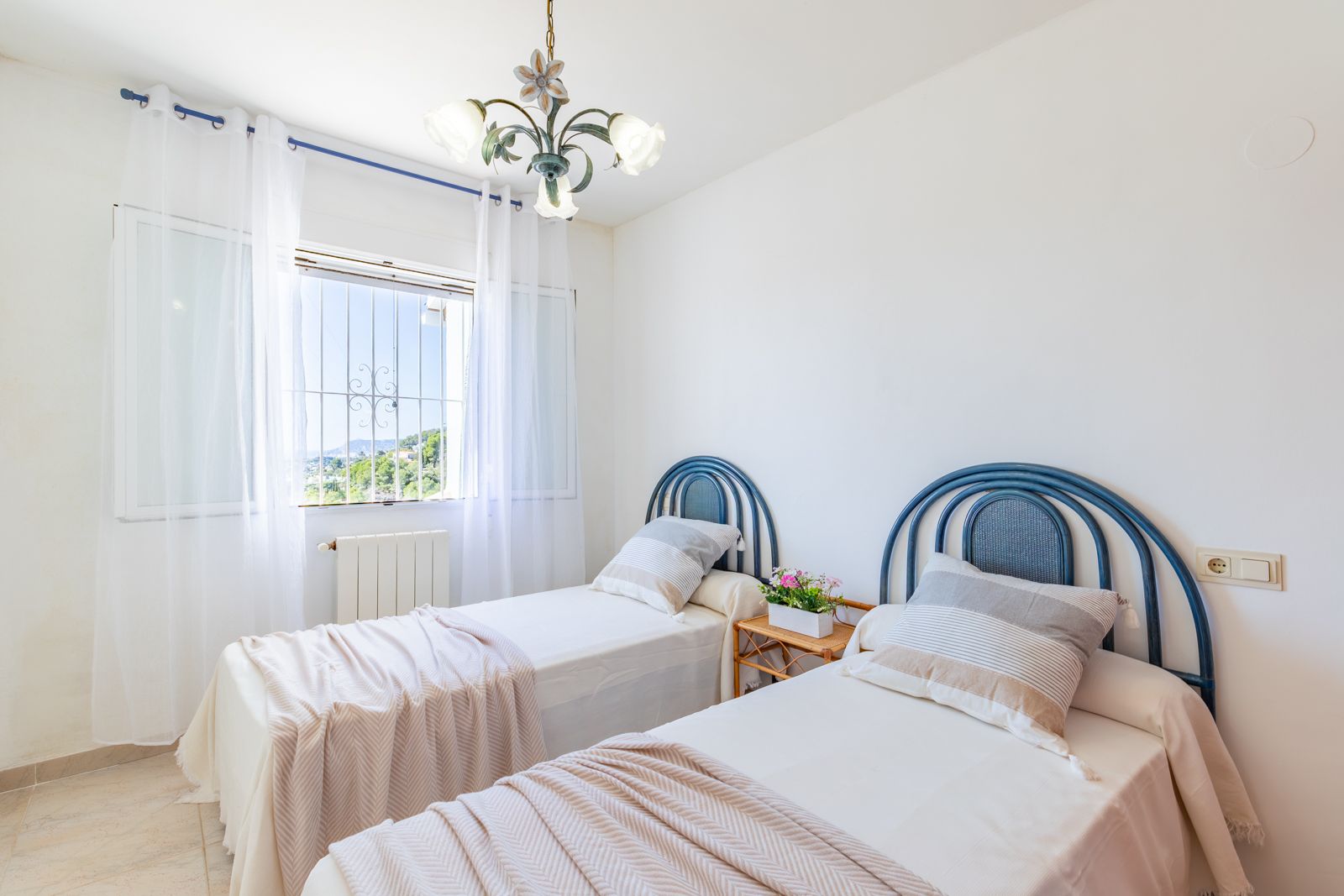 Helles Schlafzimmer mit zwei Einzelbetten, blauen Rundkopfteilen, Zentralheizung und Fenster mit Blick auf die grüne Landschaft von Moraira.