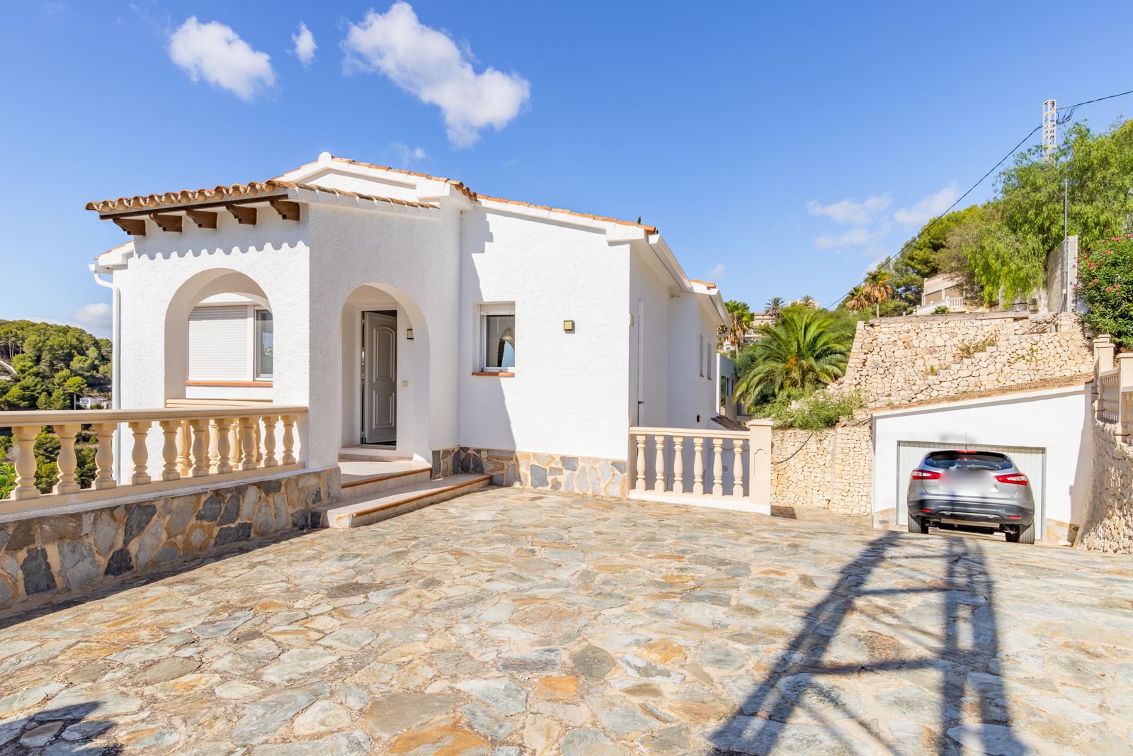 Mediterrane Außenansicht mit Rundbogeneingang, Holzbalken und großzügigem Naturstein-Hof, der zur privaten Garage und zum Haupteingang führt.