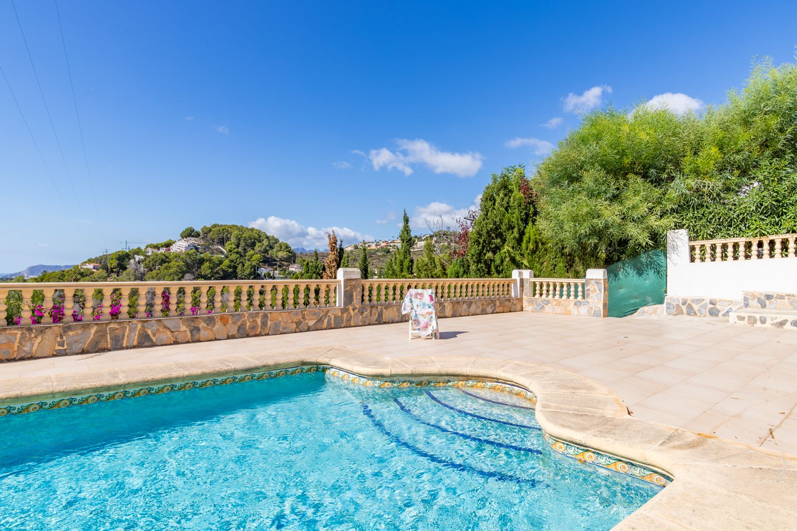 Privater Swimmingpool mit dekorativen Fliesenbordüren und weitläufiger Sonnenterrasse, begrenzt durch eine Natursteinbalustrade mit Blick auf die umliegenden Hügel.