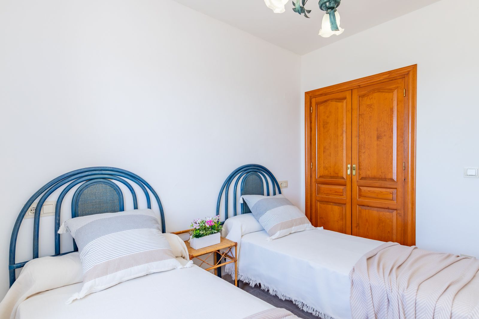 Schlafzimmer mit zwei Einzelbetten, blauen Korbkopfteilen und einem Einbauschrank aus Echtholz. Heller Raum mit weißen Wänden und praktischem Fliesenboden.