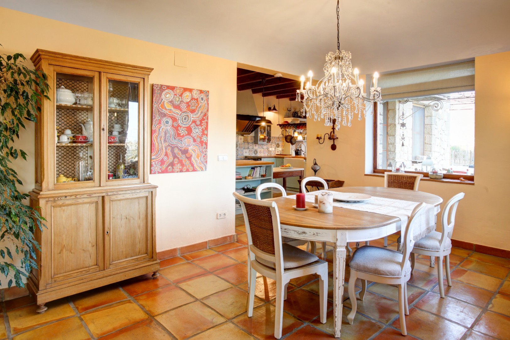 Essbereich mit Holztisch, Shabby-Chic-Stühlen und Kristallleuchter über traditionellen Terrakottafliesen und einem klassischen Vitrinenschrank.