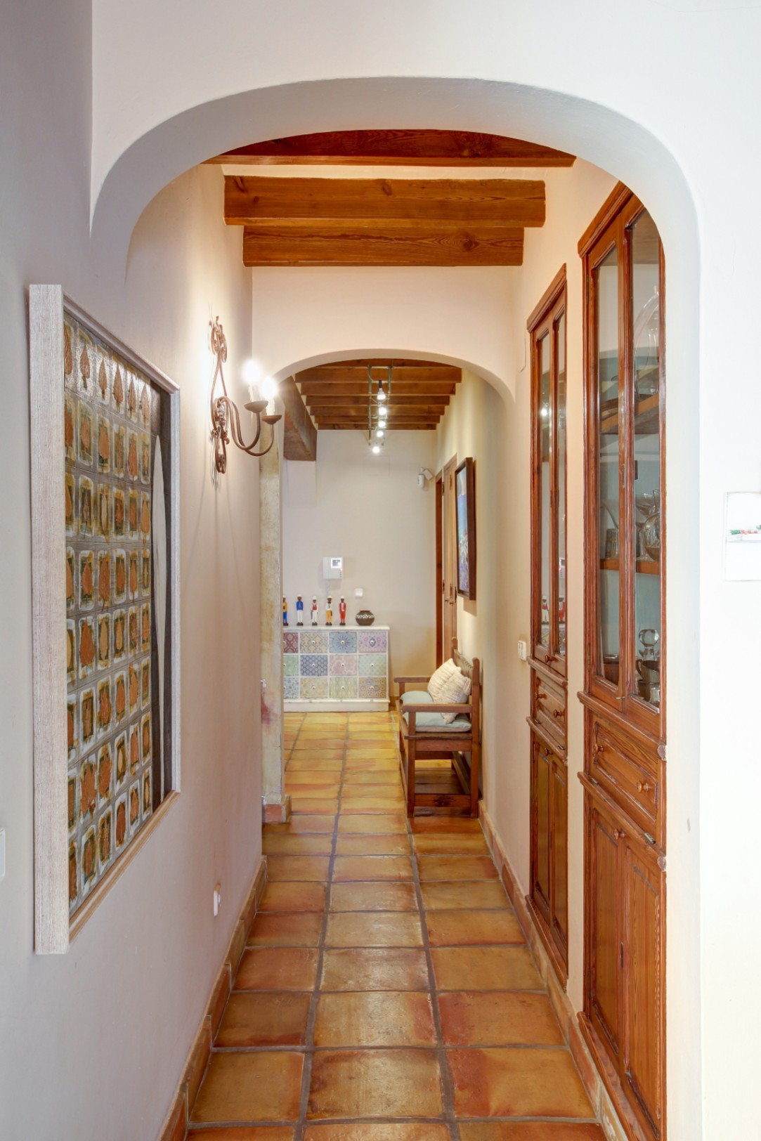 Flur mit Rundbögen, sichtbaren Holzbalken und traditionellen Terrakottafliesen. Ausgestattet mit eingebauten Holzvitrinen und rustikaler Wandbeleuchtung.