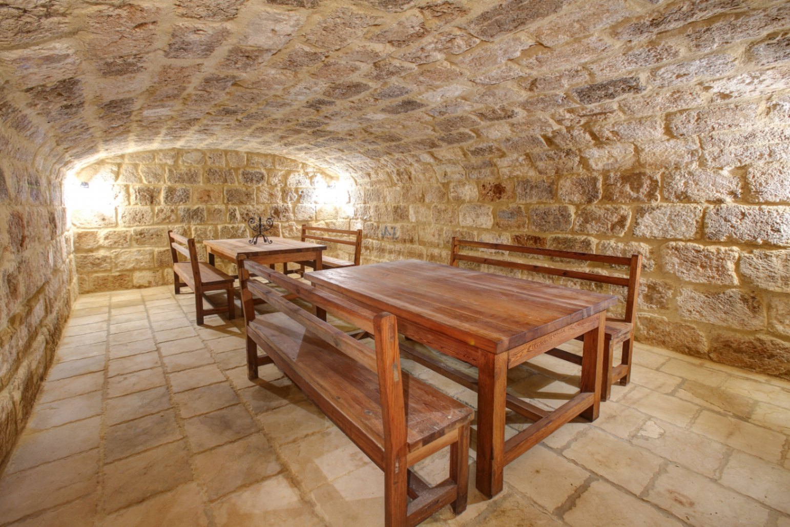 Gewölbekeller aus Naturstein mit massiven Holztischen und Bänken, traditionellem Steinboden und dezenter Wandbeleuchtung für eine rustikale Atmosphäre.