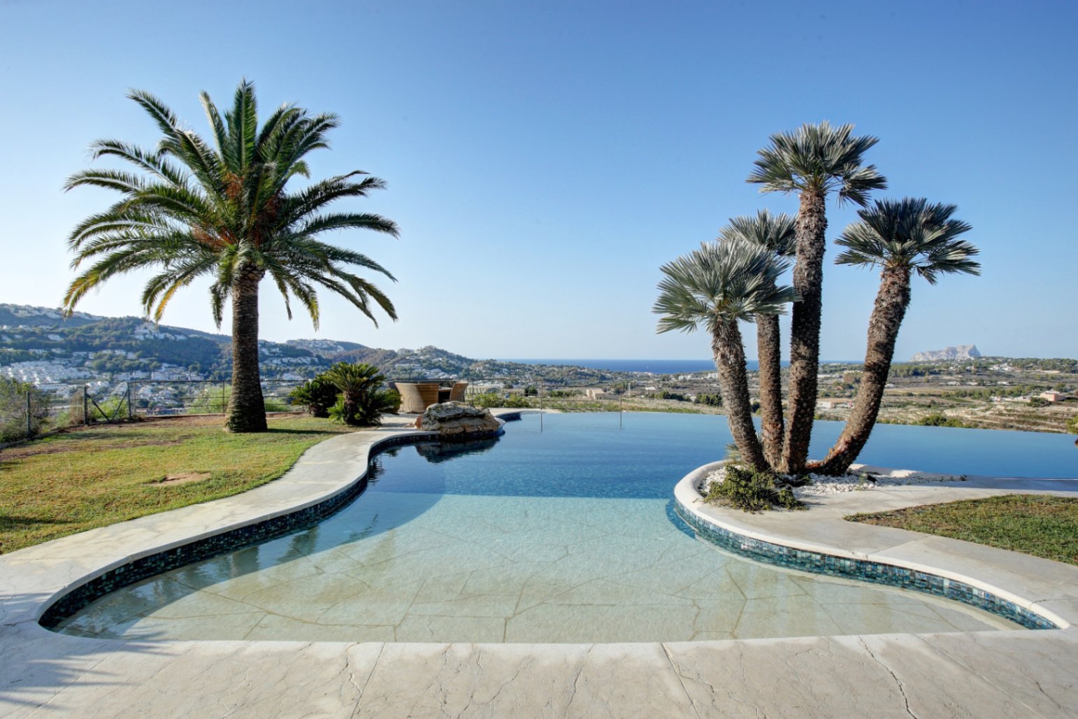 Organisch geformter Infinity-Pool, umgeben von Palmen, mit weitem Panoramablick auf das Mittelmeer und die umliegende Küstenlandschaft von Moraira.