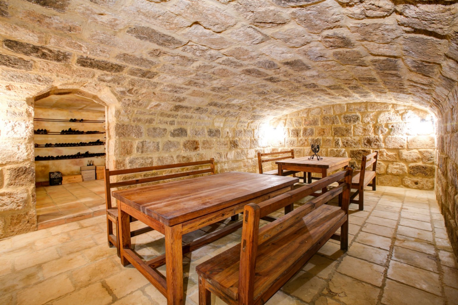Rustikaler Weinkeller mit Natursteingewölbe, Terrakottafliesen und Massivholz-Sitzgruppen sowie einem separaten Bereich für die Weinlagerung.