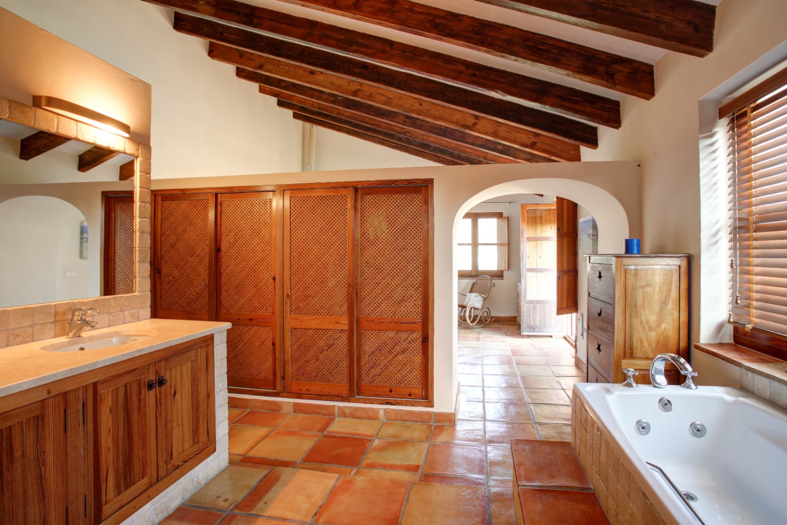 Rustikales Badezimmer mit Sichtbalkendecke, Terrakottaboden und Hydromassage-Wanne. Einbauschränke mit Holzgittertüren und ein Waschtisch mit Marmorplatte.