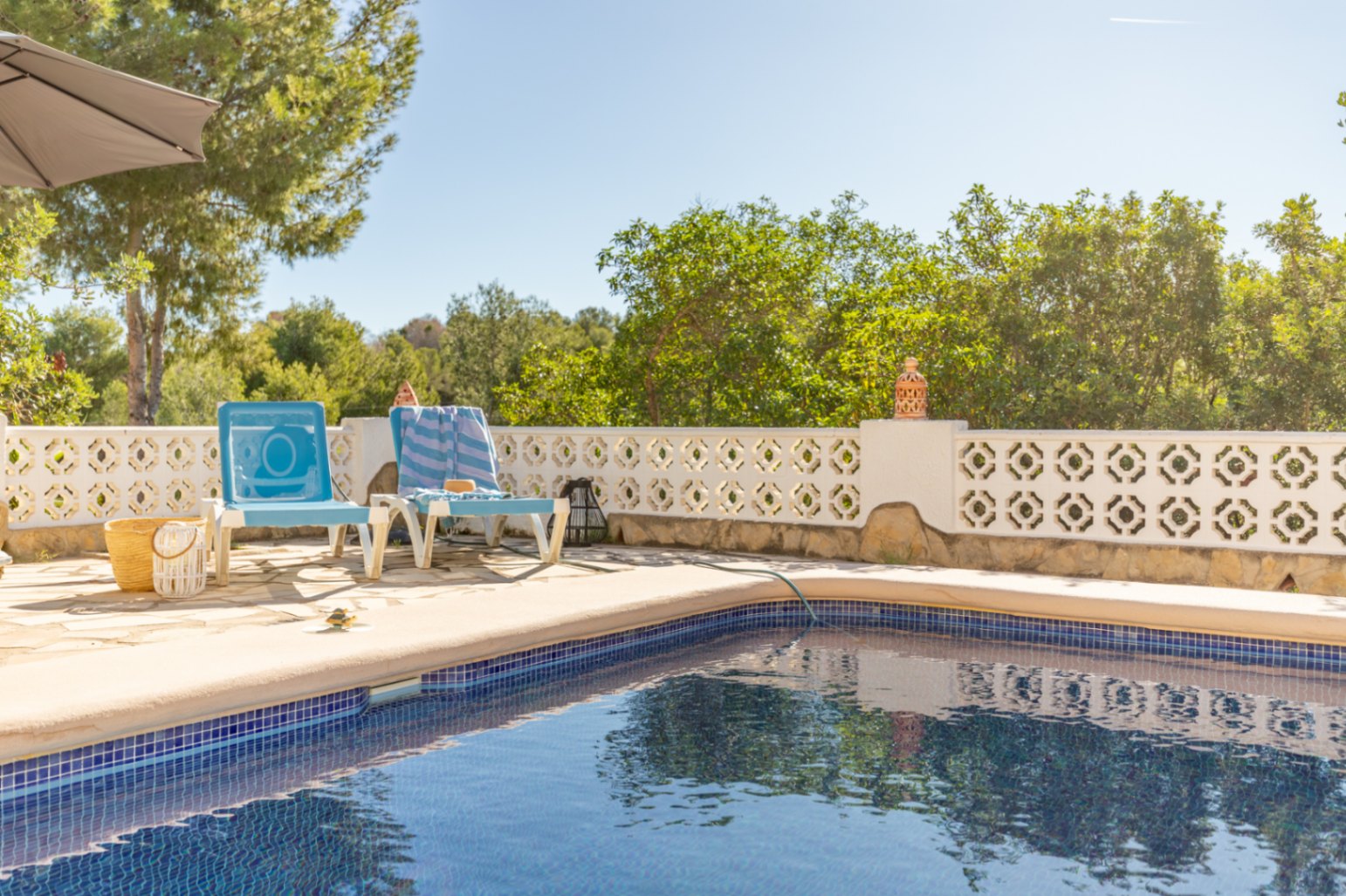 Blau gefliester Pool mit Natursteinterrasse, umrahmt von einer weißen Ziermauer und üppiger mediterraner Vegetation für maximale Privatsphäre.