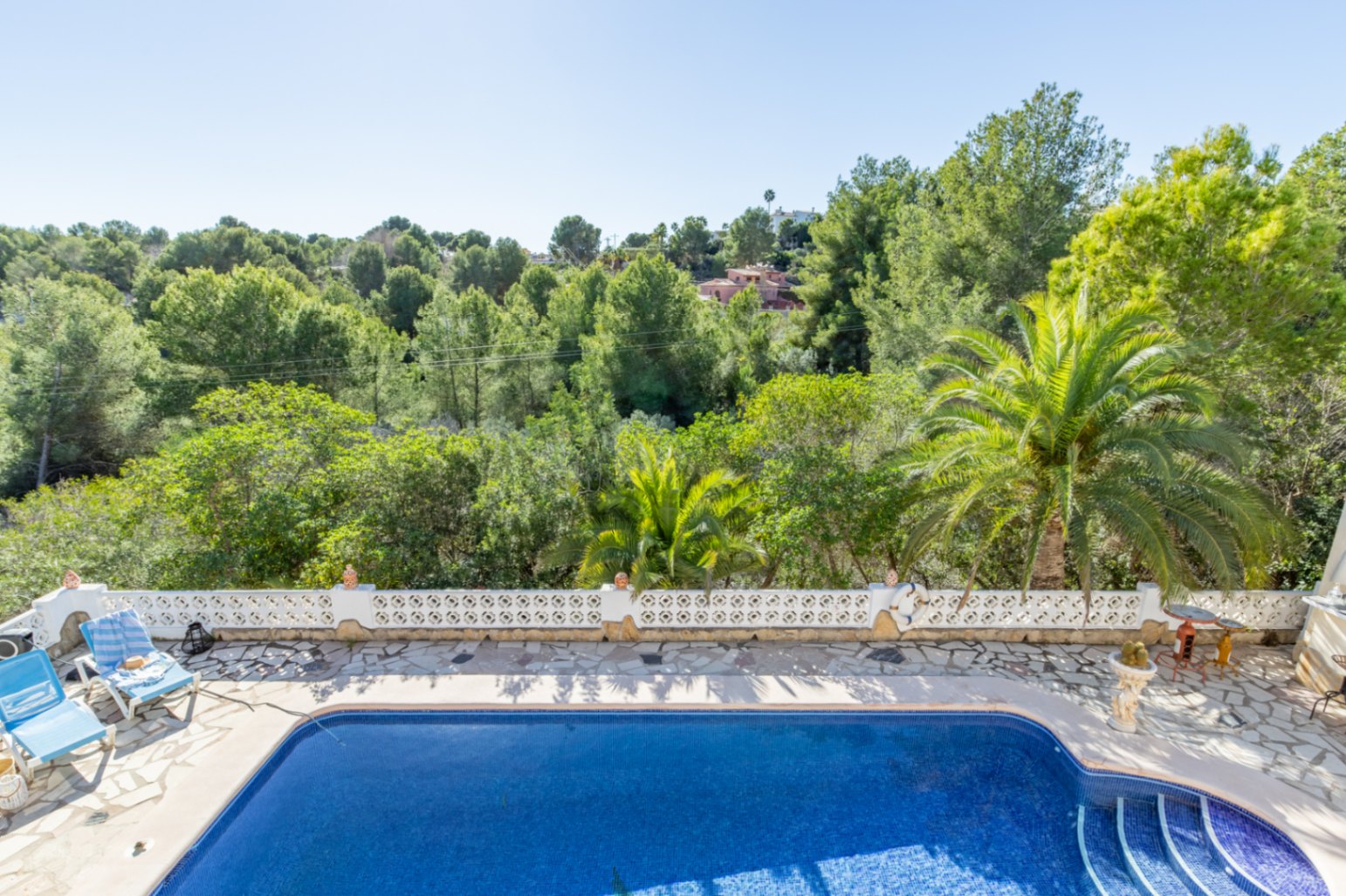 Erhöhter Blick auf den 42 m² großen Pool und die Natursteinterrasse, eingefasst von einer weißen Balustrade mit direktem Ausblick auf die angrenzende Grünzone.