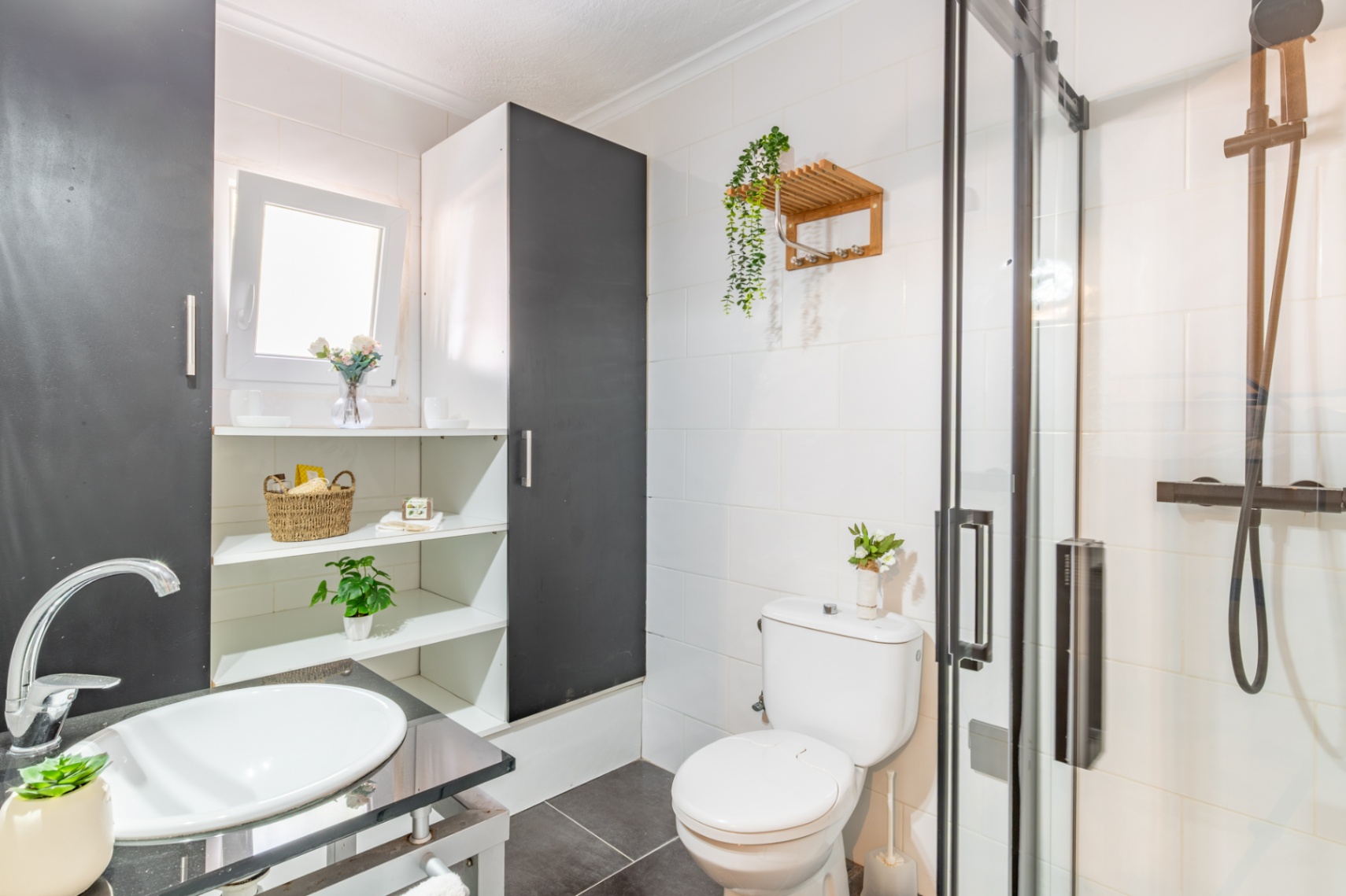 Funktionales Badezimmer mit Glasdusche, schwarzen Armaturen und weißem Aufsatzwaschbecken. Integrierte Regale und weiße Wandfliesen sorgen für Ordnung.