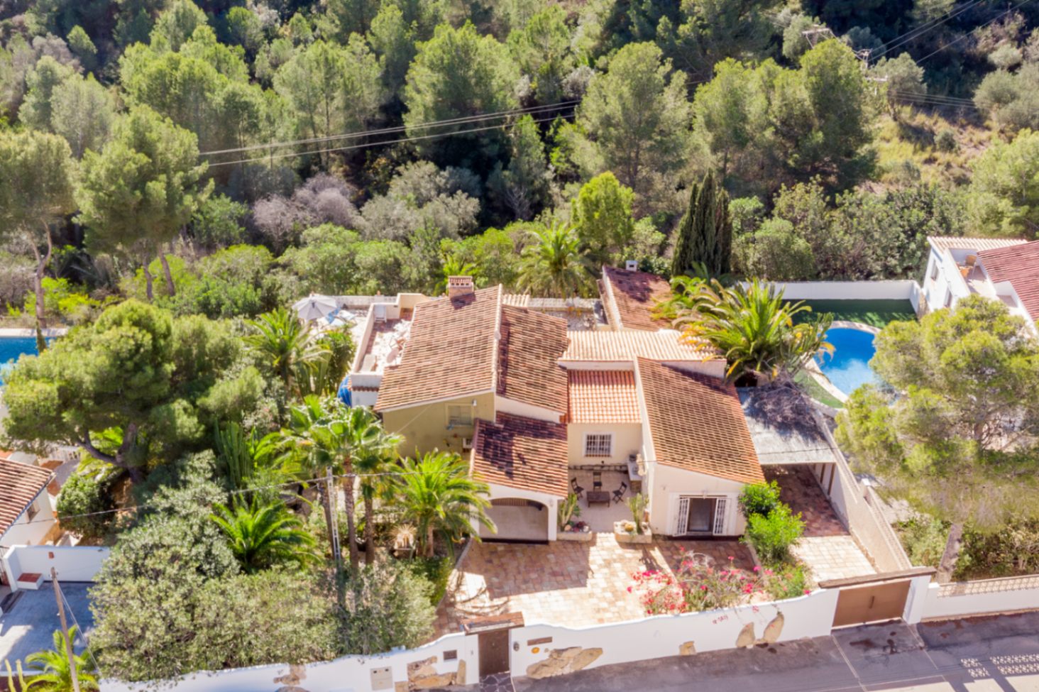 Luftaufnahme der Villa, die ihre mediterrane Architektur mit Ziegeldächern zeigt, umgeben von einer geschützten Grünzone und Palmen für maximale Privatsphäre.