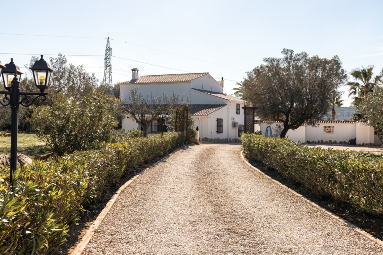 Eine von niedrigen Hecken gesäumte Kiesauffahrt führt zur weiß getünchten Fassade der Finca und unterstreicht die traditionelle Architektur und den mediterranen Garten.