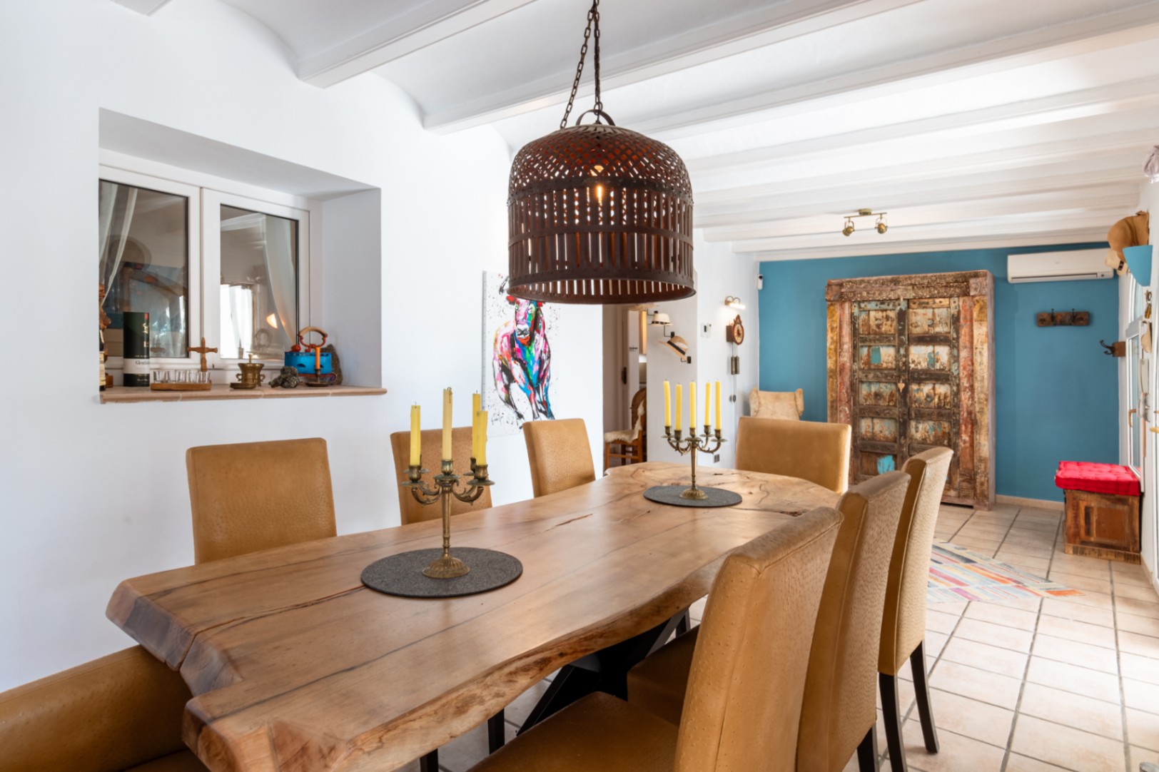 Essbereich mit massivem Baumkanten-Holztisch, strukturierten Stühlen und weißer Balkendecke, ergänzt durch eine blaue Akzentwand und rustikale Details.