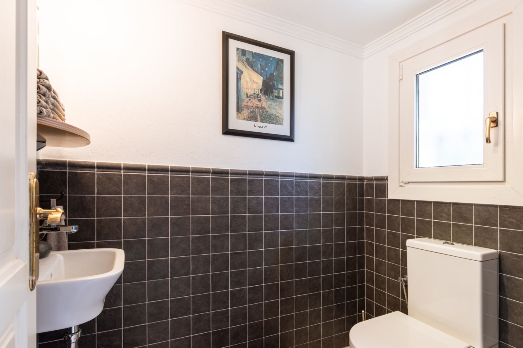 Funktionale Gästetoilette mit dunkel texturierten Wandfliesen, kompaktem Waschbecken und Dreh-Kipp-Fenster für natürliche Belüftung.
