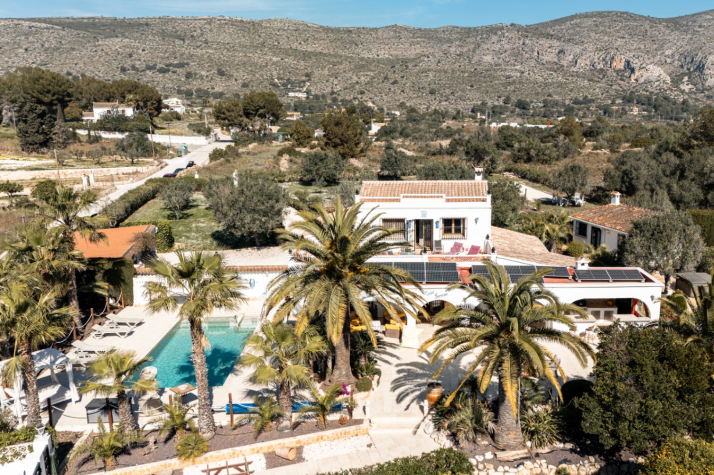 Luftaufnahme des Anwesens mit privatem Pool, Solarmodulen auf dem Dach und mediterranem Garten inmitten einer Berglandschaft.