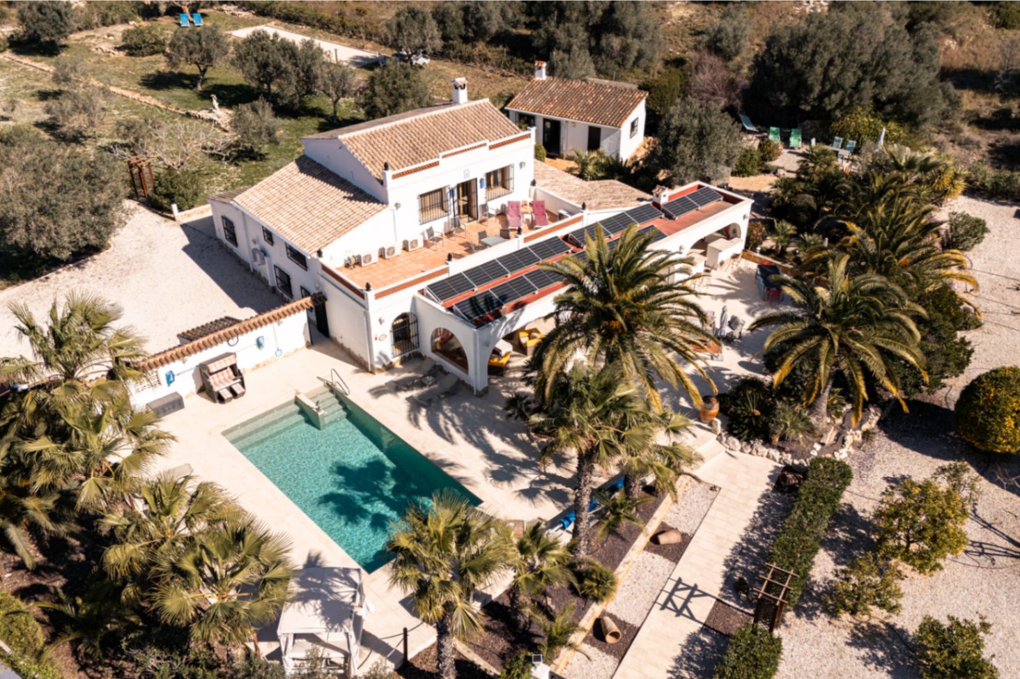 Luftbild der Finca mit rechteckigem Pool, weitläufigen Steinterrassen und Solaranlage auf der Naya, eingebettet in einen gepflegten mediterranen Garten.