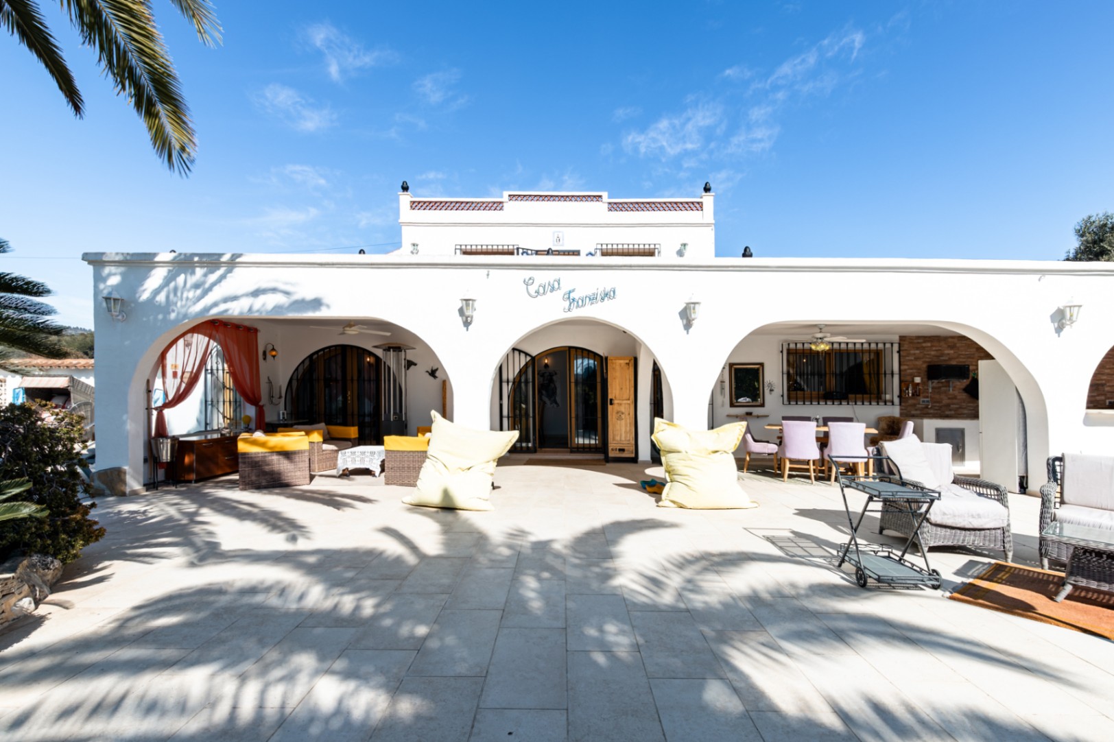 Mediterrane weiße Fassade mit bogenförmiger Naya, gepflasterter Terrasse und Außenwohnbereichen unter dem Namenszug "Casa Franziska".