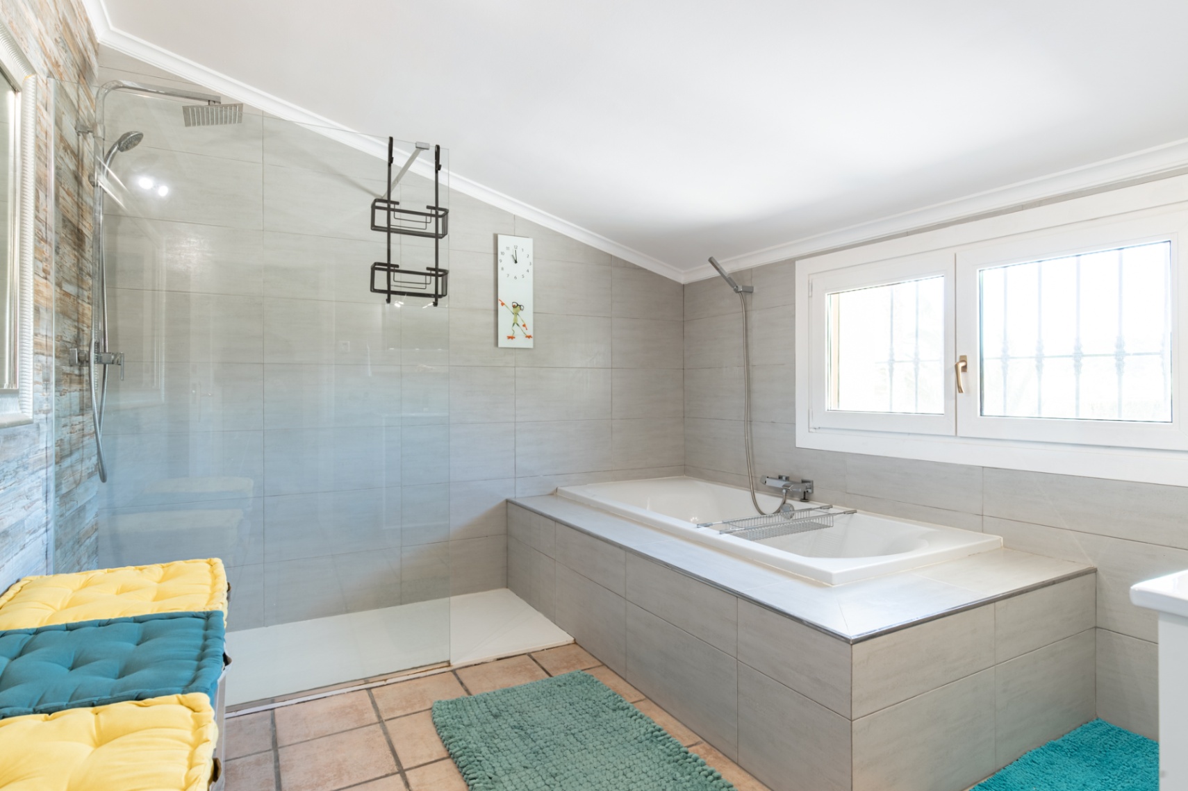 Modernes Badezimmer mit begehbarer Dusche, Glastrennwand und Einbaubadewanne. Ausgestattet mit grauen Wandfliesen, Chromarmaturen und einem Fenster für Tageslicht.