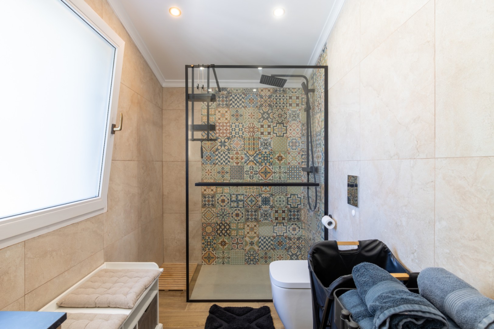 Modernes Badezimmer mit begehbarer Dusche, markanter Rückwand aus gemusterten Fliesen, schwarzer Duschabtrennung und Bodenbelag in Holzoptik.