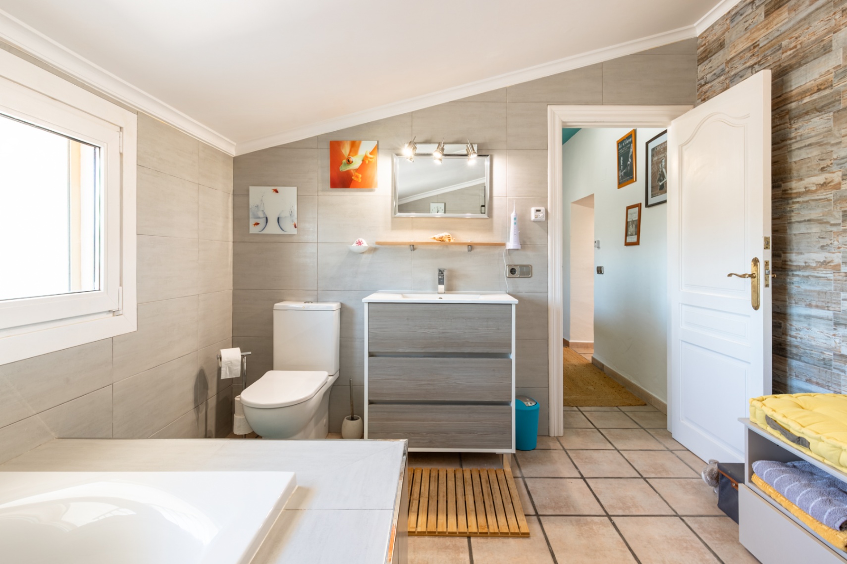 Modernisiertes Badezimmer mit Dachschräge, Waschtisch in Holzoptik und großformatigen Wandfliesen sowie einer dekorativen Akzentwand aus Stein.