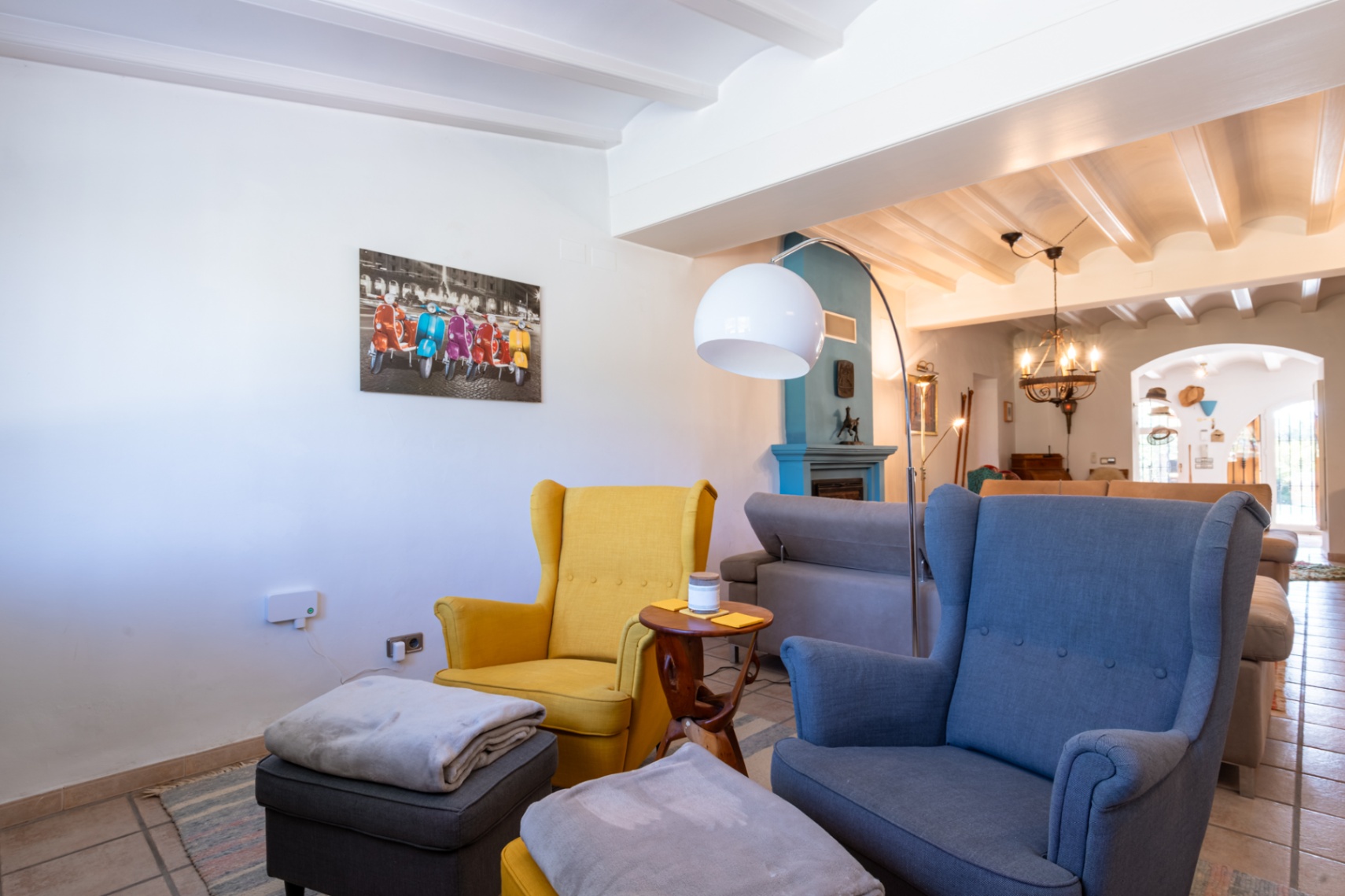 Wohnzimmer mit weißen Balkendecken, blauem Kamin und farbenfrohen Ohrensesseln, ergänzt durch eine moderne Bogenlampe.