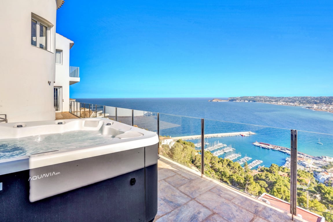 Außen-Whirlpool der Marke Aquavia Spa auf einer Steinterrasse mit Glasgeländer und Panoramablick auf den Hafen von Jávea und das Mittelmeer.
