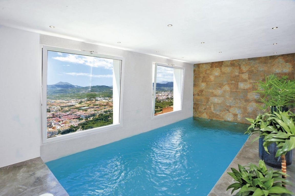 Beheiztes Hallenbad mit Panoramafenstern und Blick auf die Berge, ausgestattet mit einer Natursteinwand, Einbaustrahlern und direktem Tageslicht.