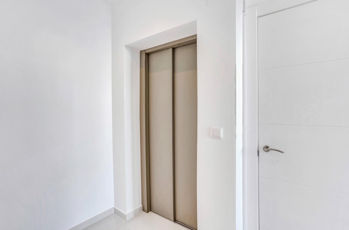 Der private Aufzug mit bronzefarbenen Metalltüren ist in einen minimalistischen Flur mit weißen Wänden und passenden Innentüren integriert.