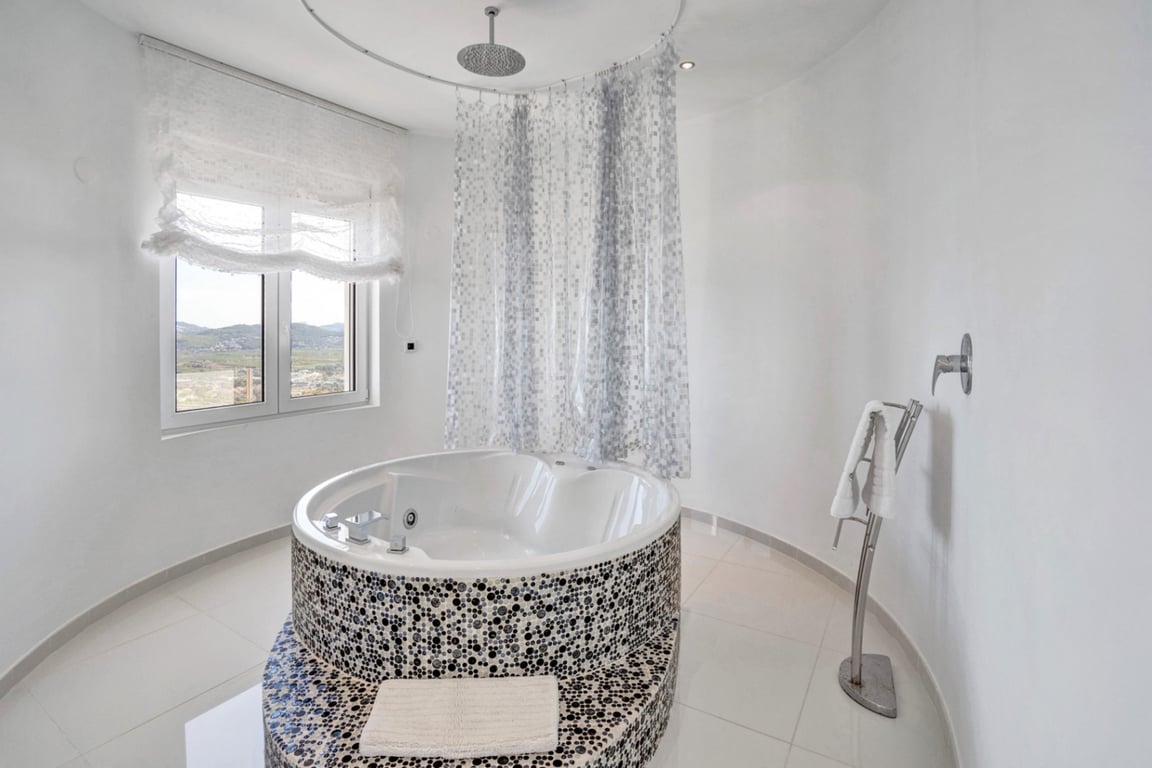 Design-Badezimmer mit runder, mosaikverzierter Whirlpool-Badewanne, integrierter Regendusche und Fenster mit Bergblick.