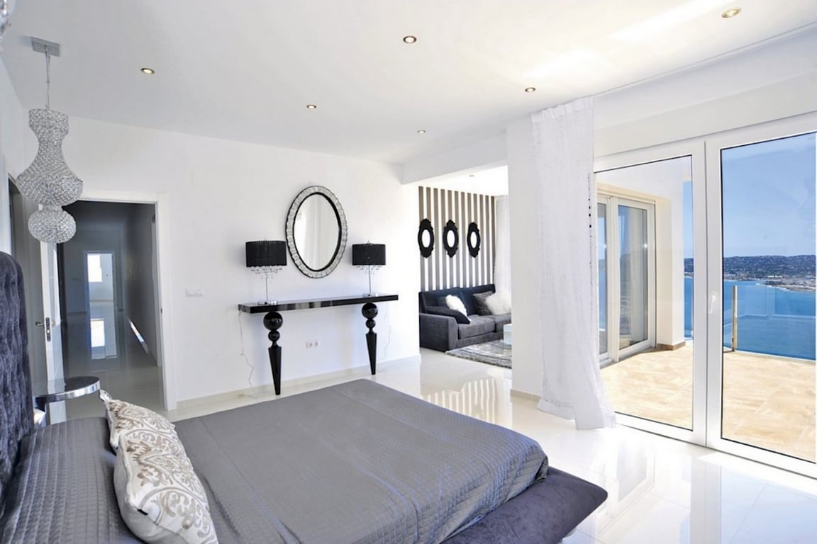Hauptschlafzimmer mit weißen Hochglanzböden, integriertem Wohnbereich und direktem Zugang zur Terrasse mit weitem Blick über das Mittelmeer.