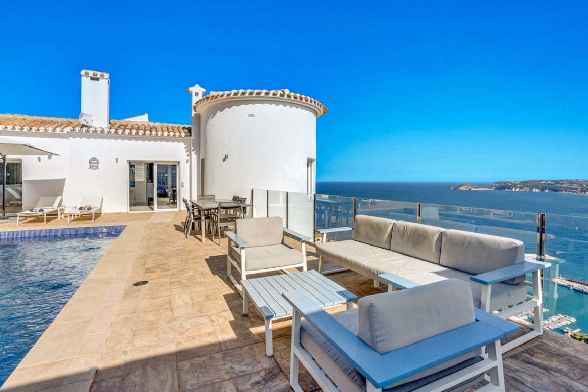 Hauptterrasse mit Lounge-Bereich, Essplatz und Pool, die durch Glasgeländer einen Panoramablick auf den Hafen von Jávea und das Mittelmeer bietet.