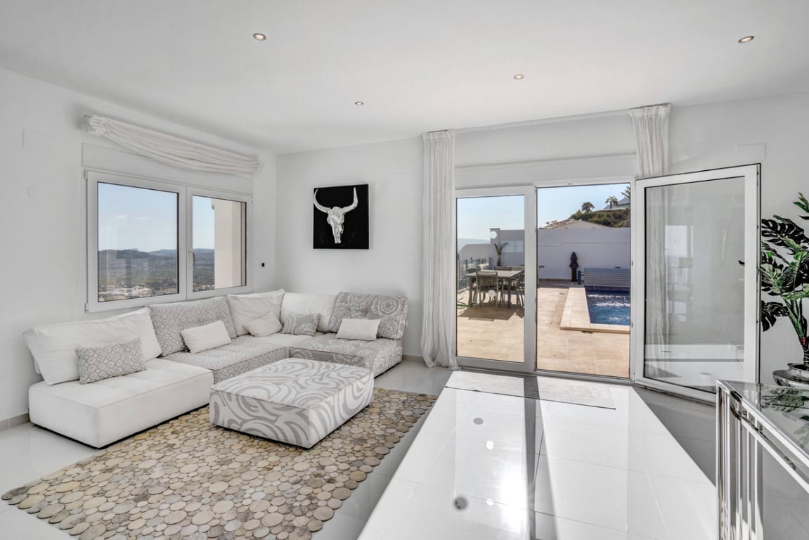 Heller Wohnbereich mit modularem Sofa und direktem Zugang zur Poolterrasse, die einen weiten Blick auf das Meer und die Berge bietet.